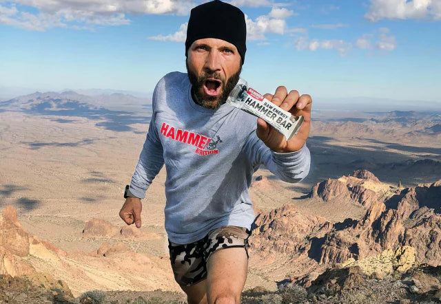 Trail runner on a desert summit holding up a Hammer Bar